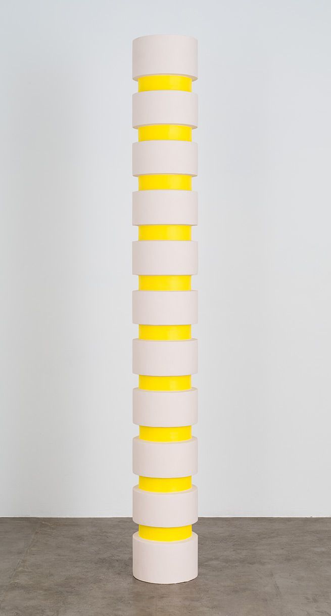 a tall white and yellow vase sitting on top of a cement floor