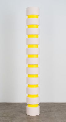 a tall white and yellow vase sitting on top of a cement floor