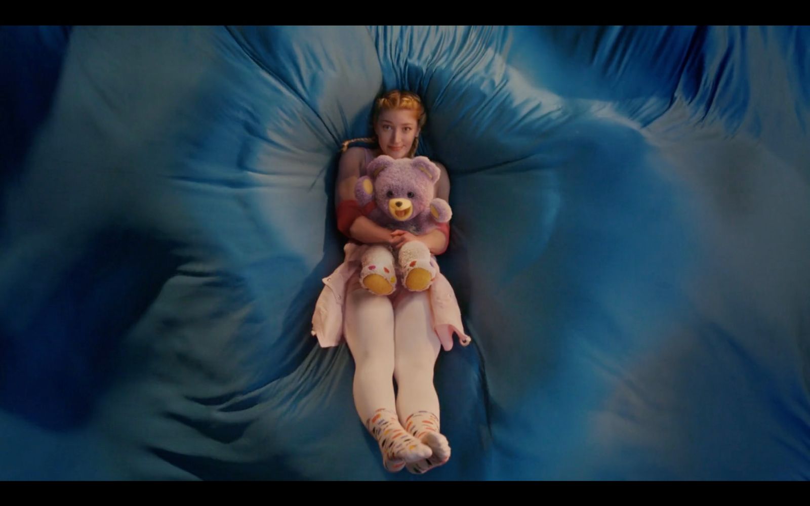 a girl laying on a bed with a teddy bear