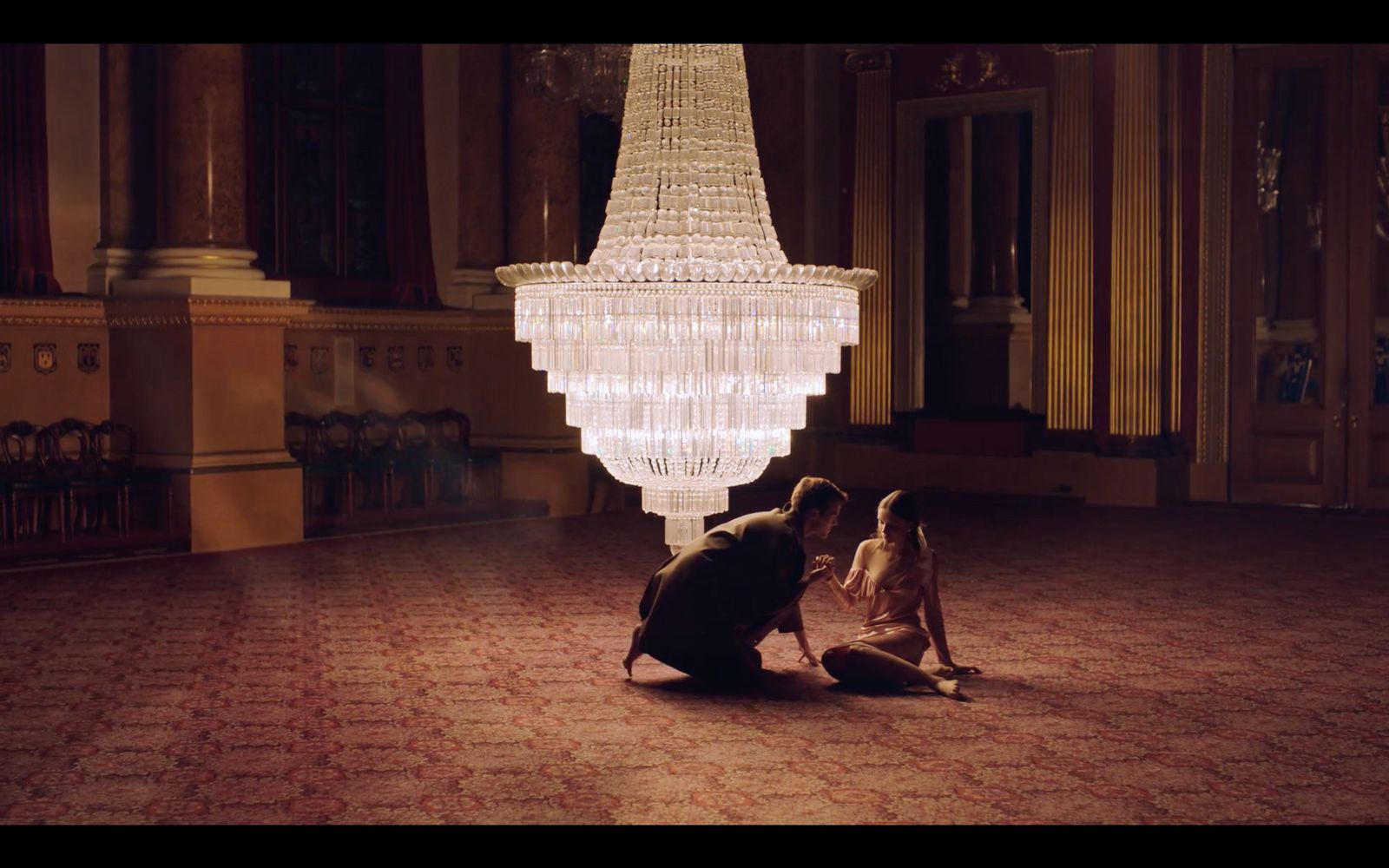 a man kneeling down next to a woman under a chandelier