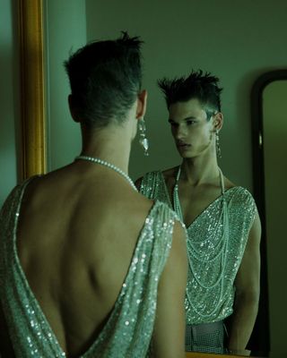 a man in a silver dress looking at himself in a mirror