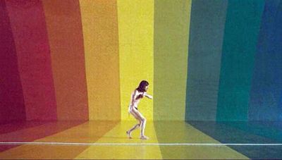 a woman is walking in front of a rainbow colored wall