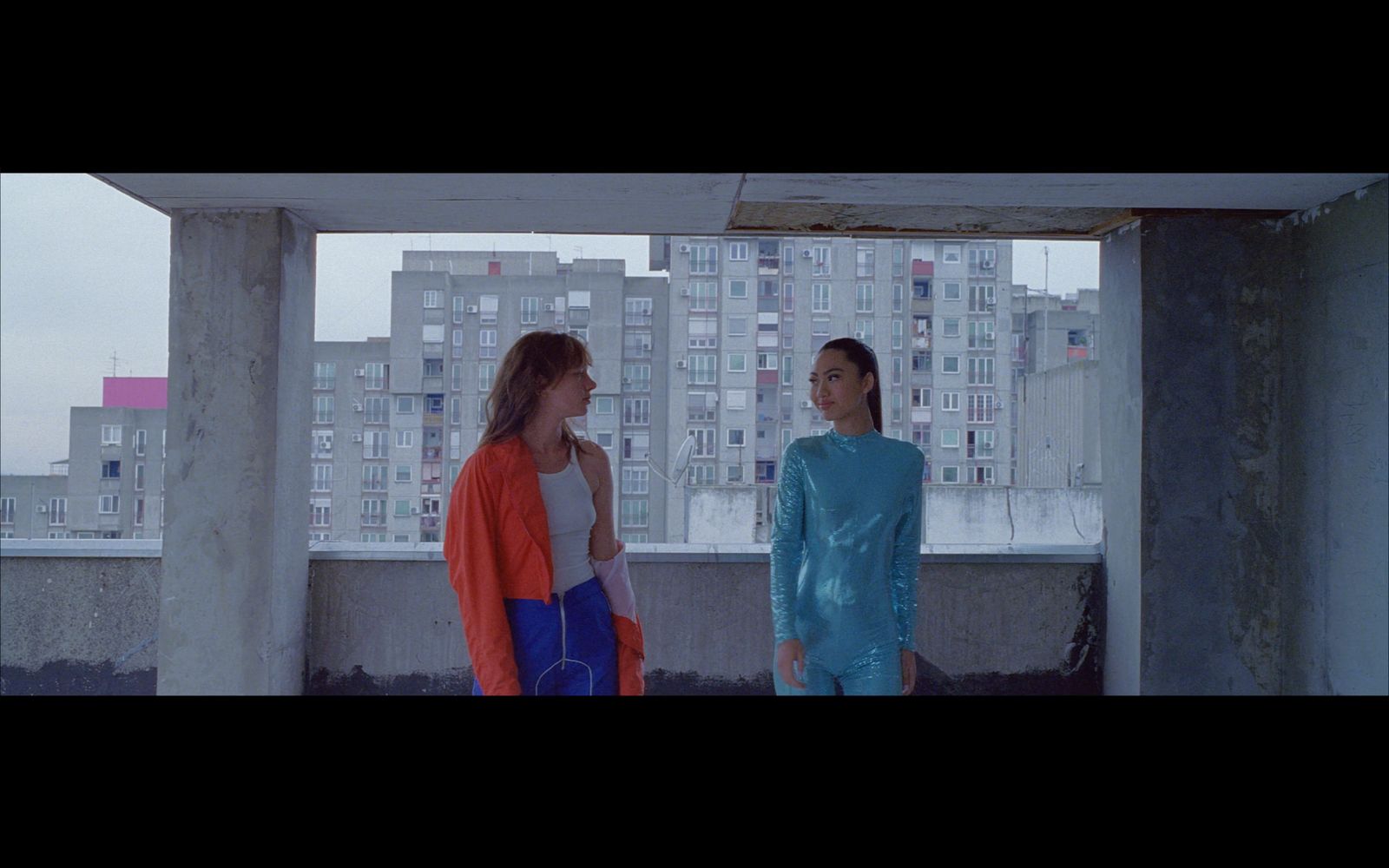 two women standing on a balcony in front of a city