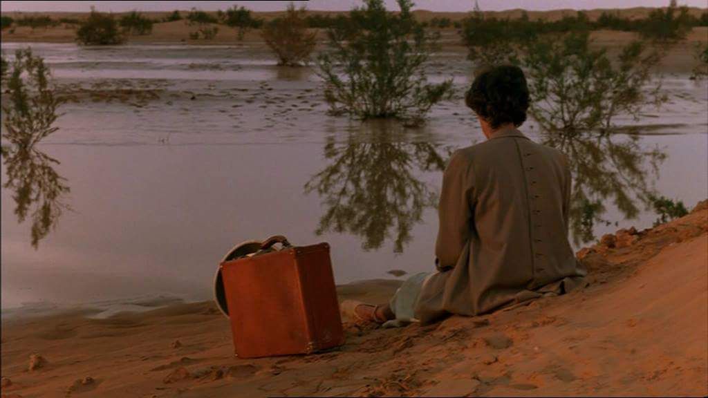 a man sitting on a beach next to a body of water