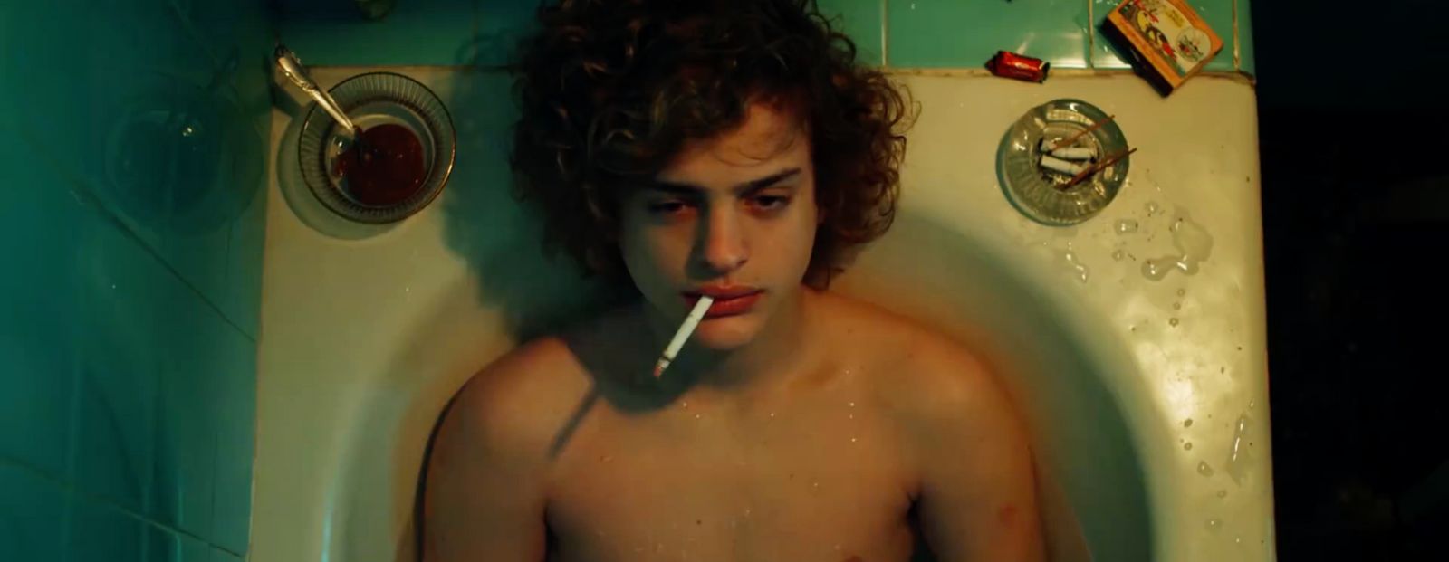 a shirtless man smoking a cigarette in a bathtub