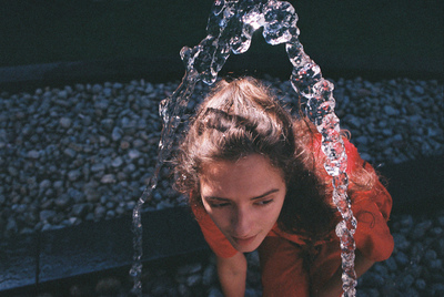 a woman in a red shirt is under a water fountain