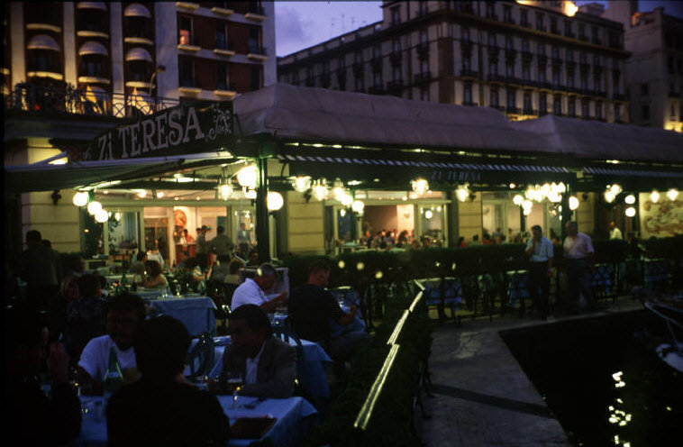 a group of people sitting outside of a restaurant at night