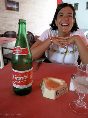 a woman sitting at a table with a bottle of wine and cheese