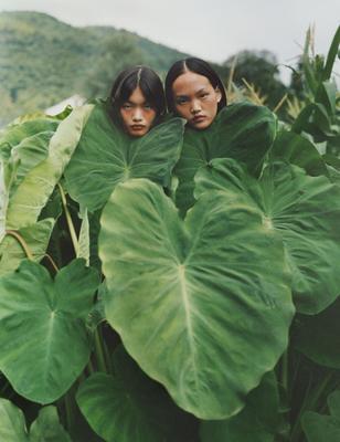 two young girls are hiding behind large leaves