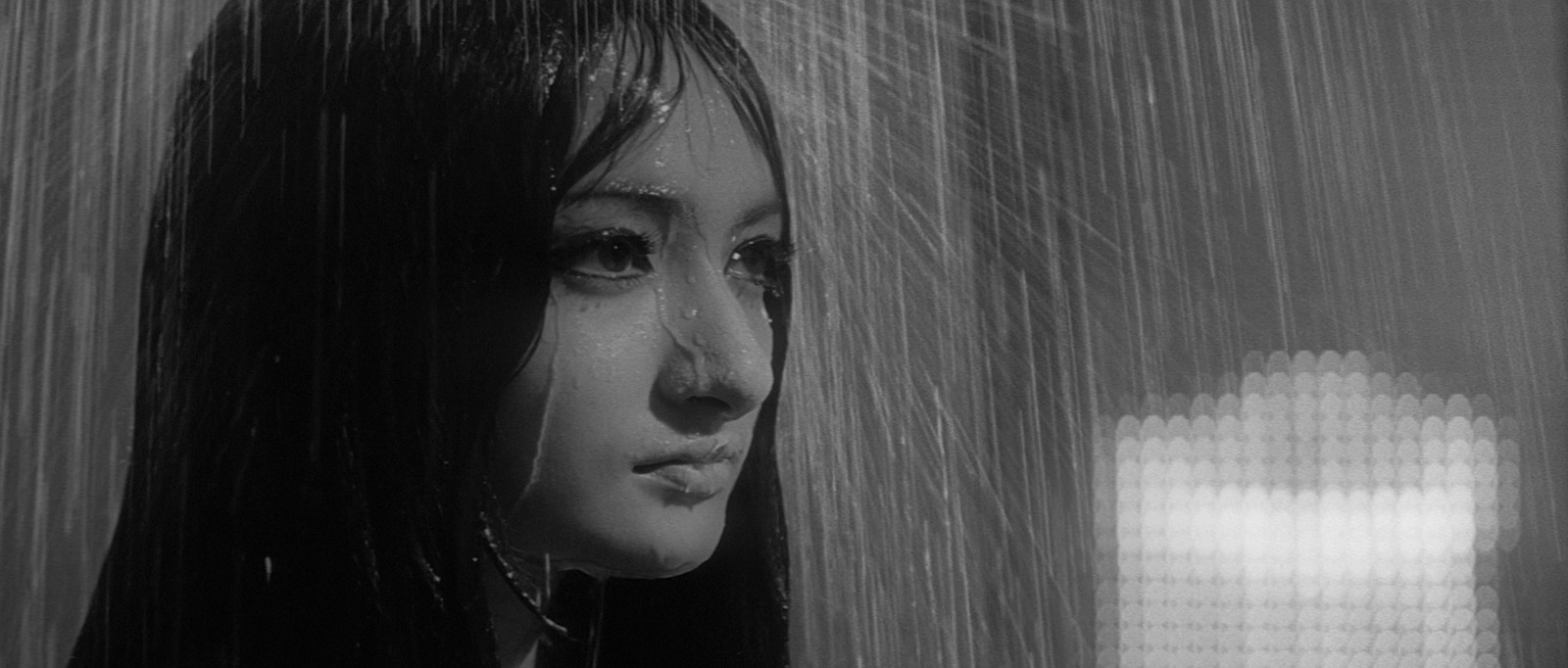 a woman standing under a rain shower in a black and white photo