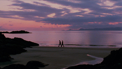 two people walking on a beach at sunset