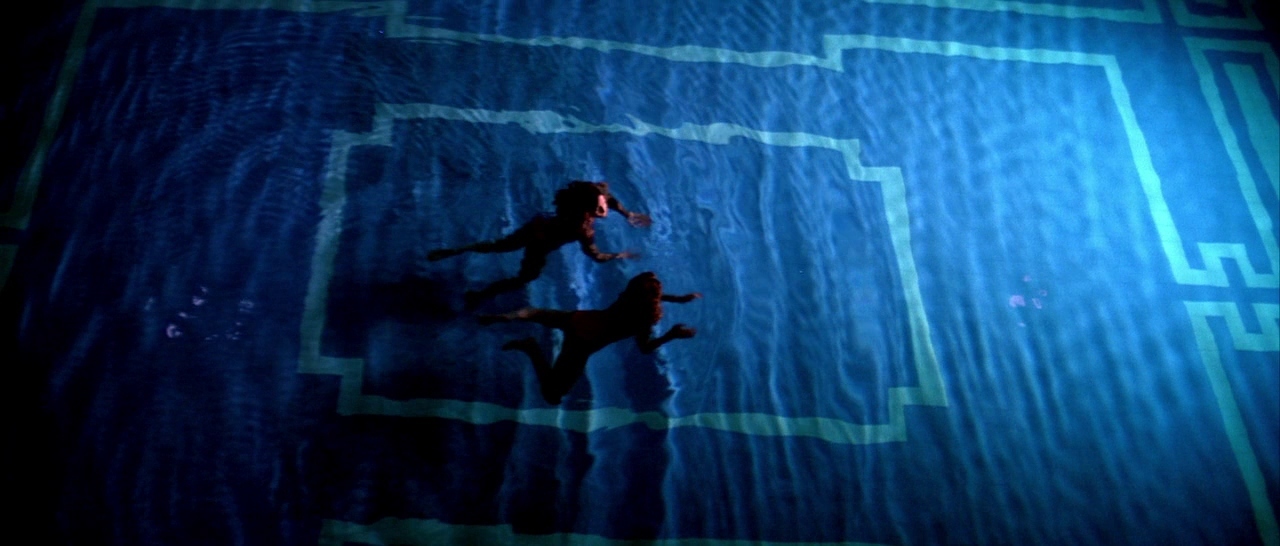 two people are swimming in a pool at night