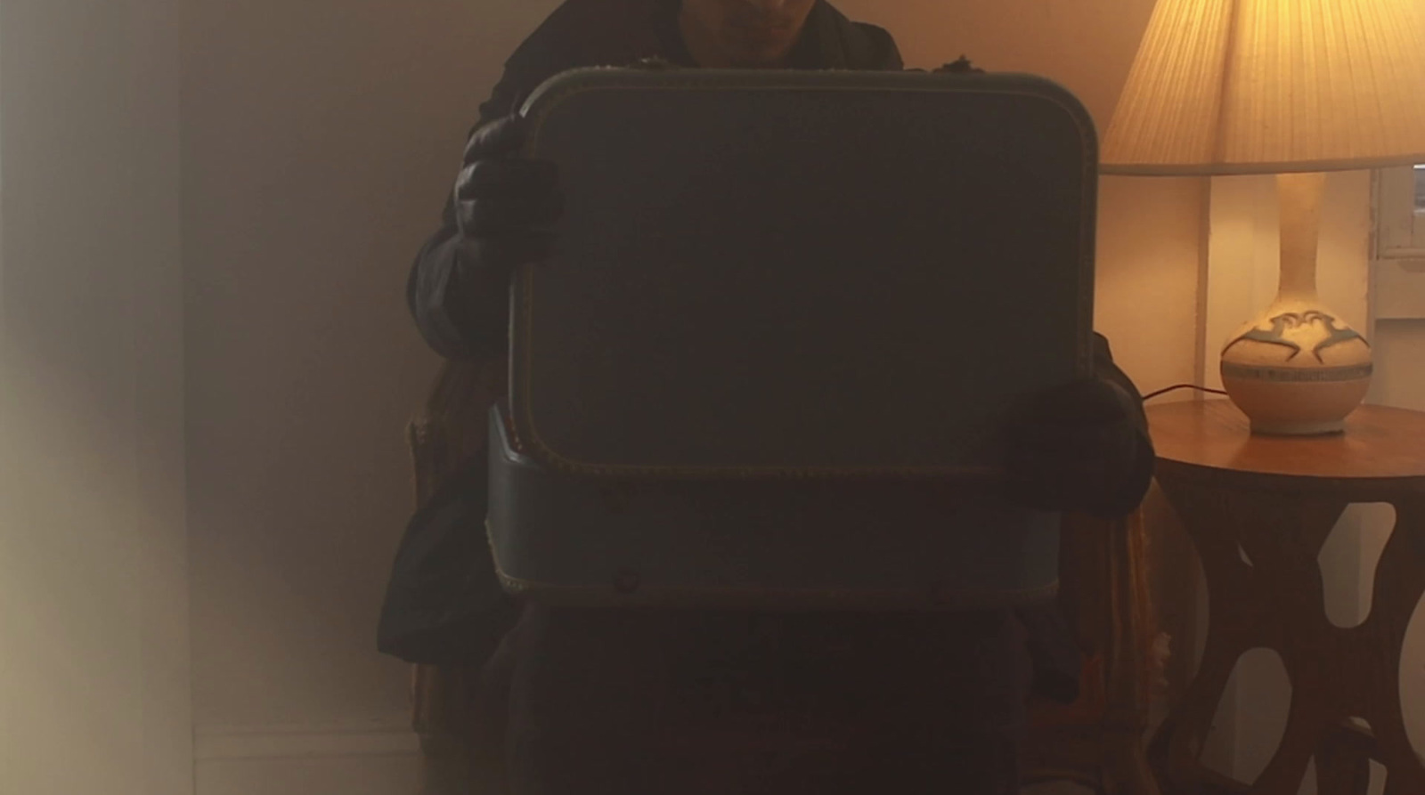 a woman holding a piece of luggage next to a lamp