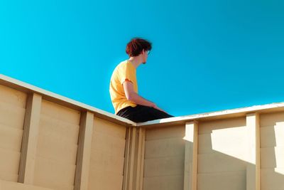 a person sitting on a wall with a blue sky in the background