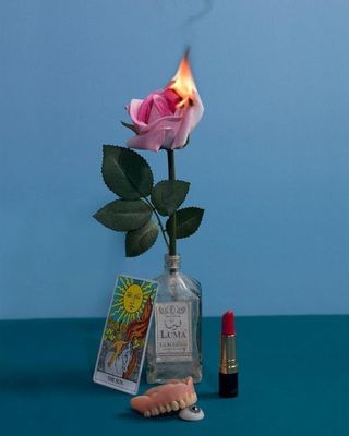 a pink rose sitting in a bottle next to a lipstick