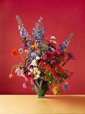 a green vase filled with lots of colorful flowers