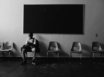 a man sitting in a row of chairs in front of a blackboard