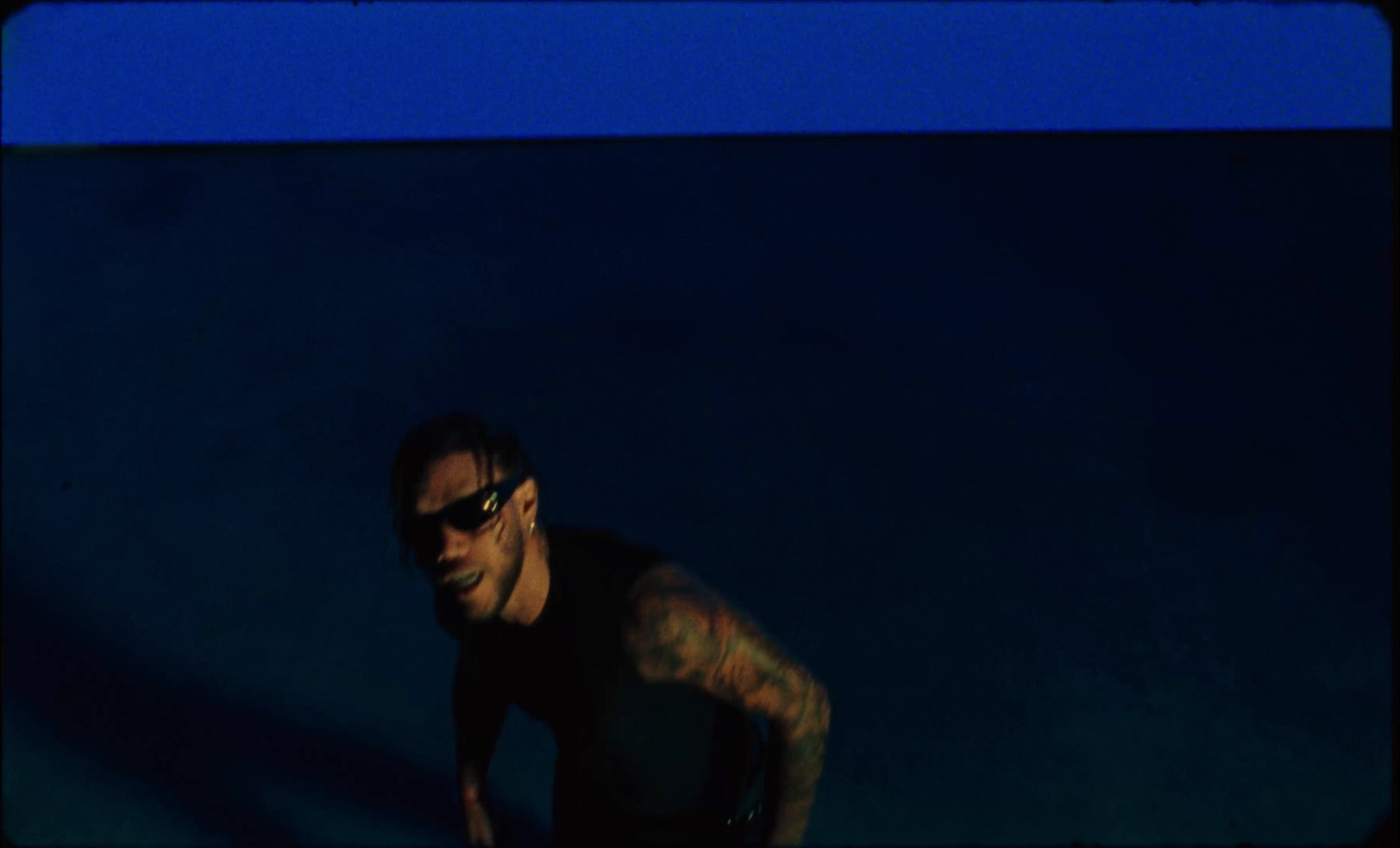 a man with tattoos and sunglasses standing in the dark