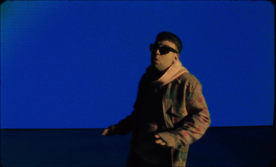 a man wearing sunglasses standing in front of a blue background