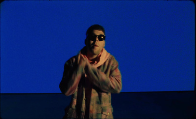 a man wearing sunglasses standing in front of a blue background