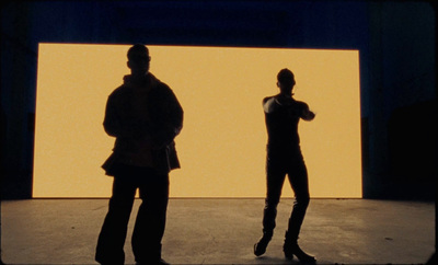 two people standing in front of a yellow wall