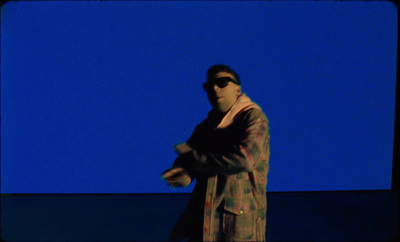 a man wearing sunglasses and a coat standing in front of a blue background