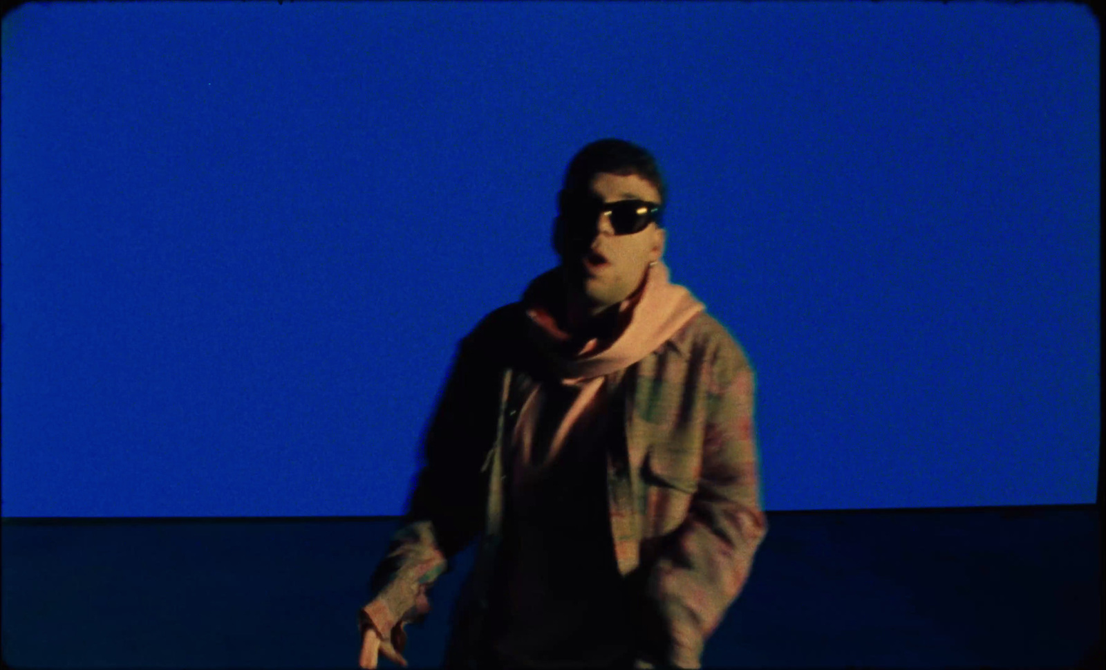 a man wearing sunglasses and a scarf standing in front of a blue background