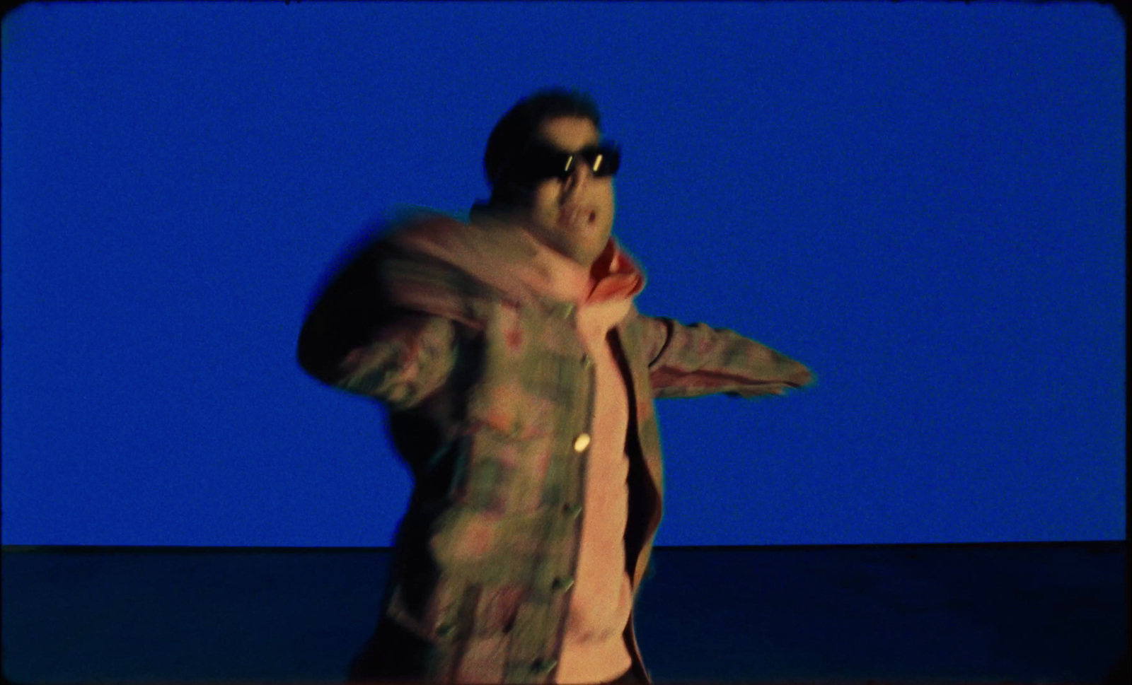 a man in a jacket and sunglasses standing in front of a blue background