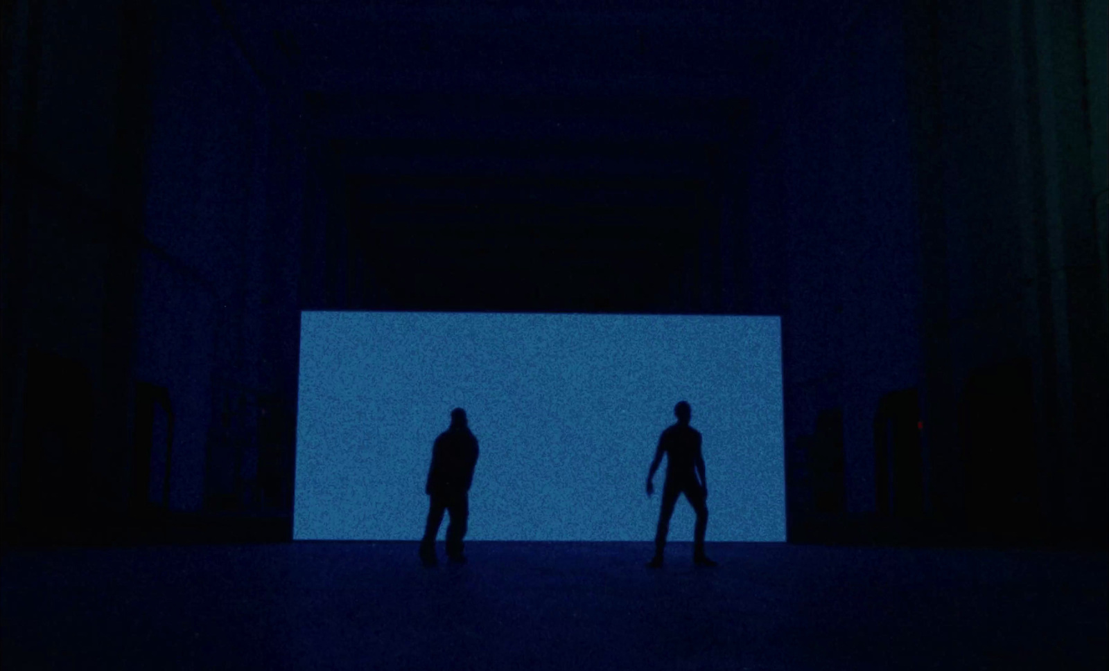 two people standing in front of a large screen in a dark room