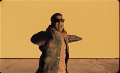 a man in a jacket and sunglasses standing in front of a yellow wall