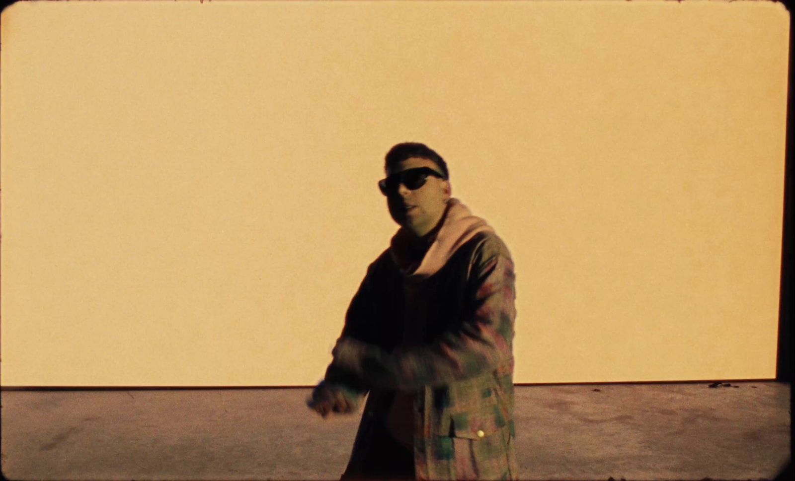 a man in a coat and sunglasses walking down a street