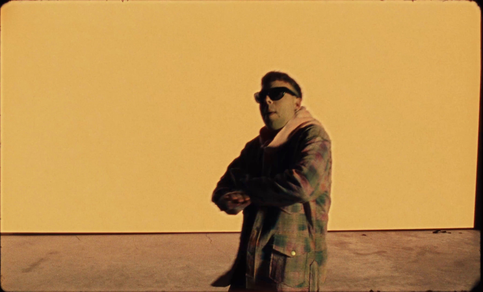 a man in a coat and sunglasses standing in front of a yellow wall