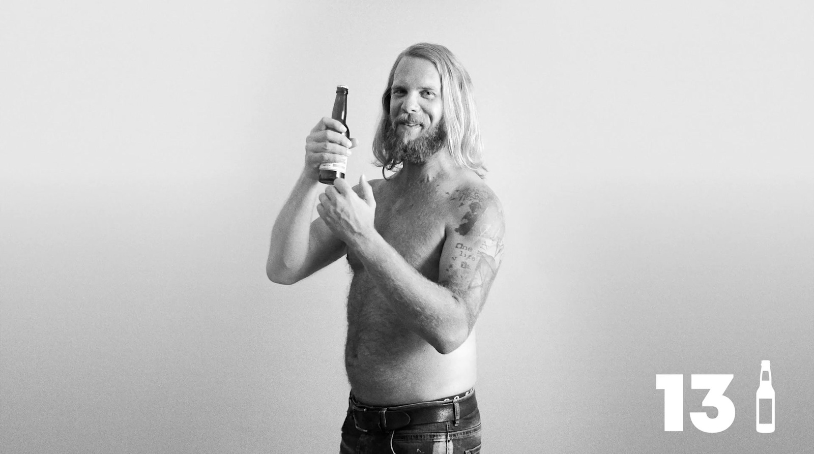 a shirtless man holding a beer and a cell phone