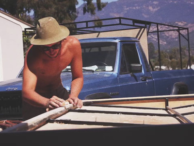 a shirtless man working on a wooden boat