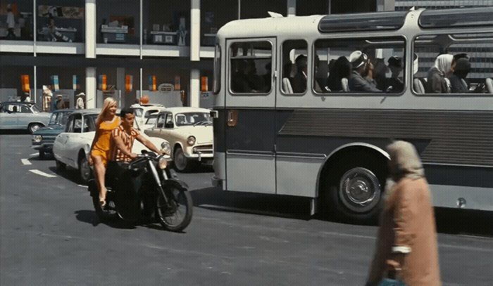 a woman riding a motorcycle down a street next to a bus