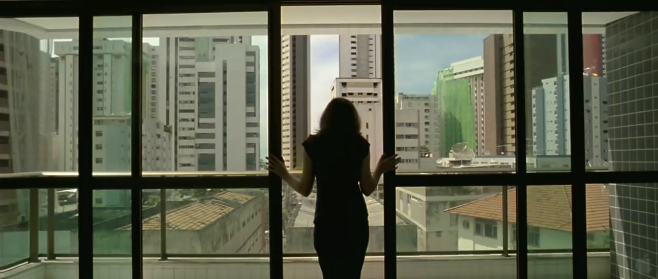 a woman standing in front of a window looking out at a city