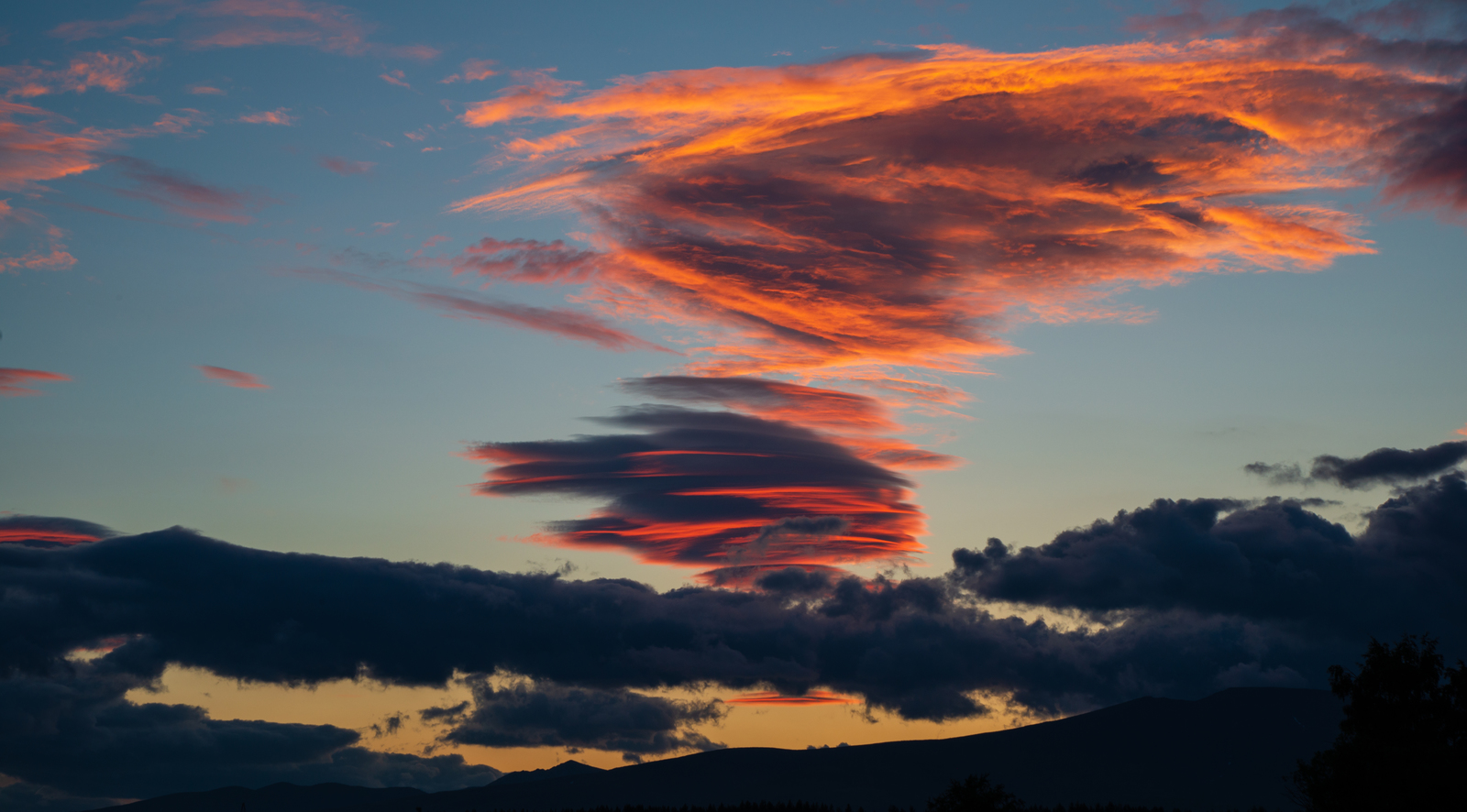 a red cloud is in the sky above a mountain