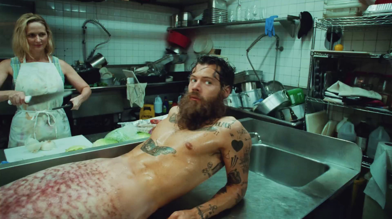 a man with a beard and tattoos sitting in a kitchen sink