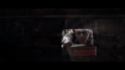 a man with glasses looking through a hole in a brick wall