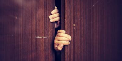 a person's hand peeking through a wooden door