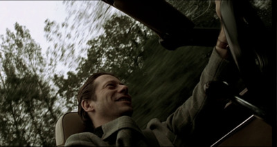 a man driving a car with trees in the background