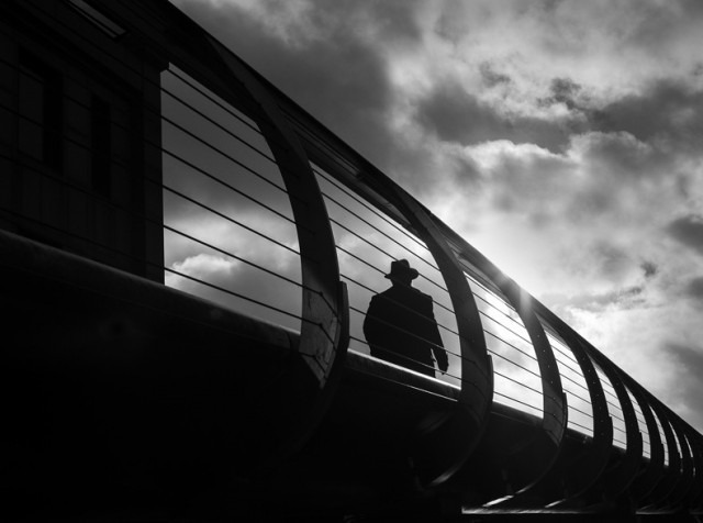 a black and white photo of a man standing on a bridge