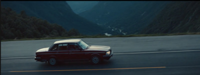 a red car driving down a road next to mountains