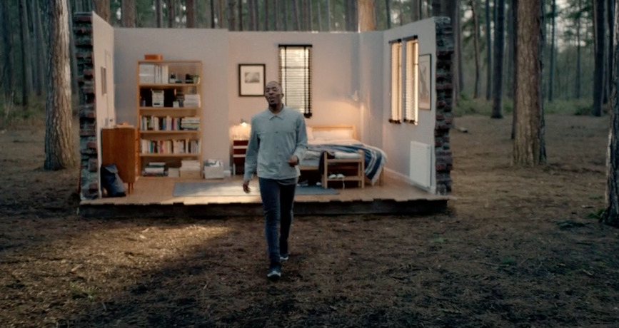 a man standing outside of a tiny house in the woods