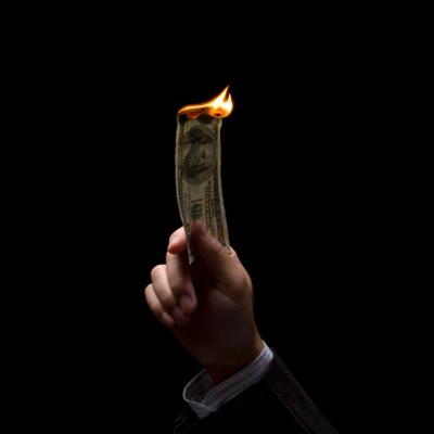 a hand holding a burning dollar bill