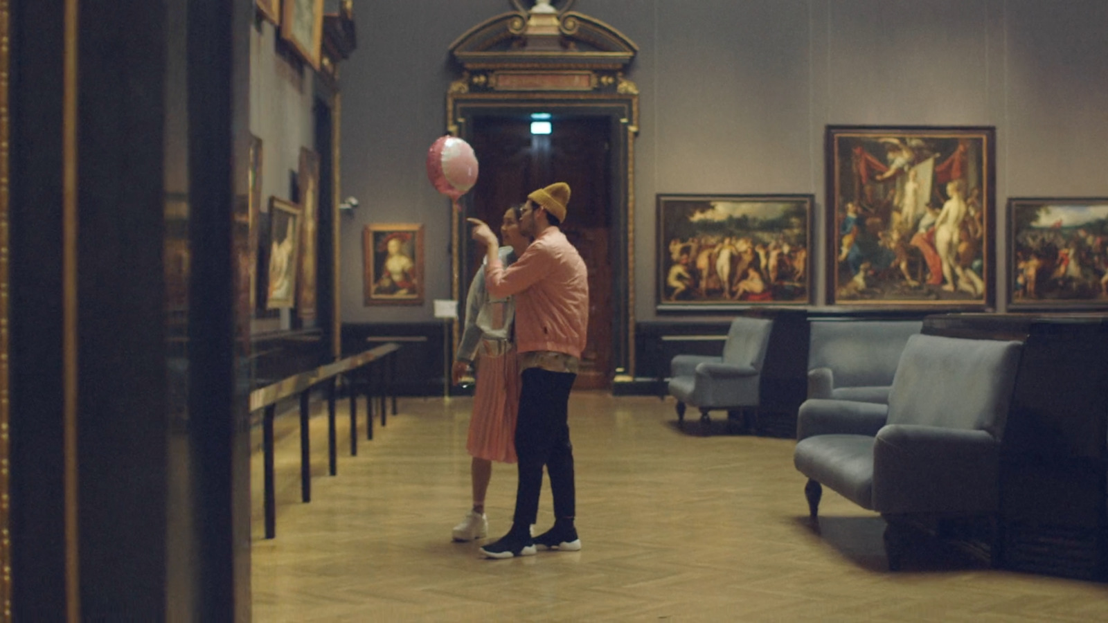 a man and a woman standing in a room with paintings on the walls