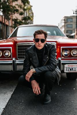 a man sitting on the ground next to a red car