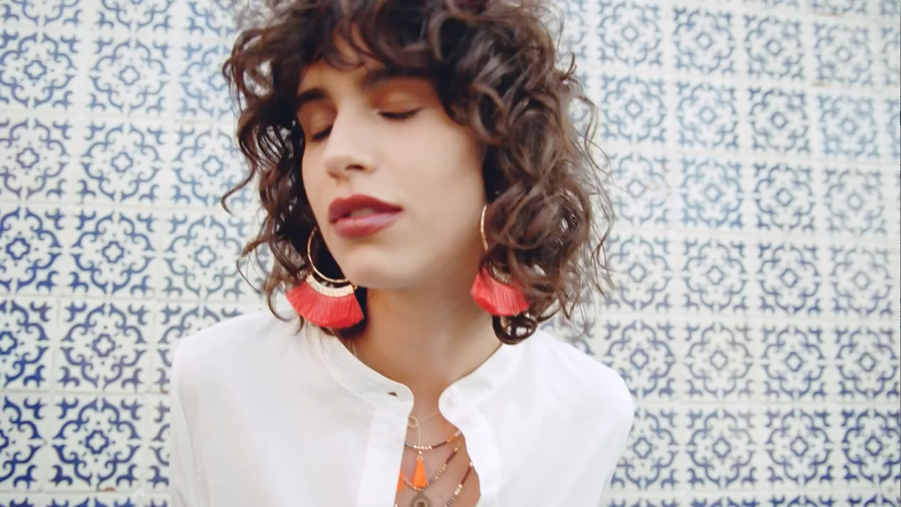 a woman with curly hair wearing a white shirt and orange earrings