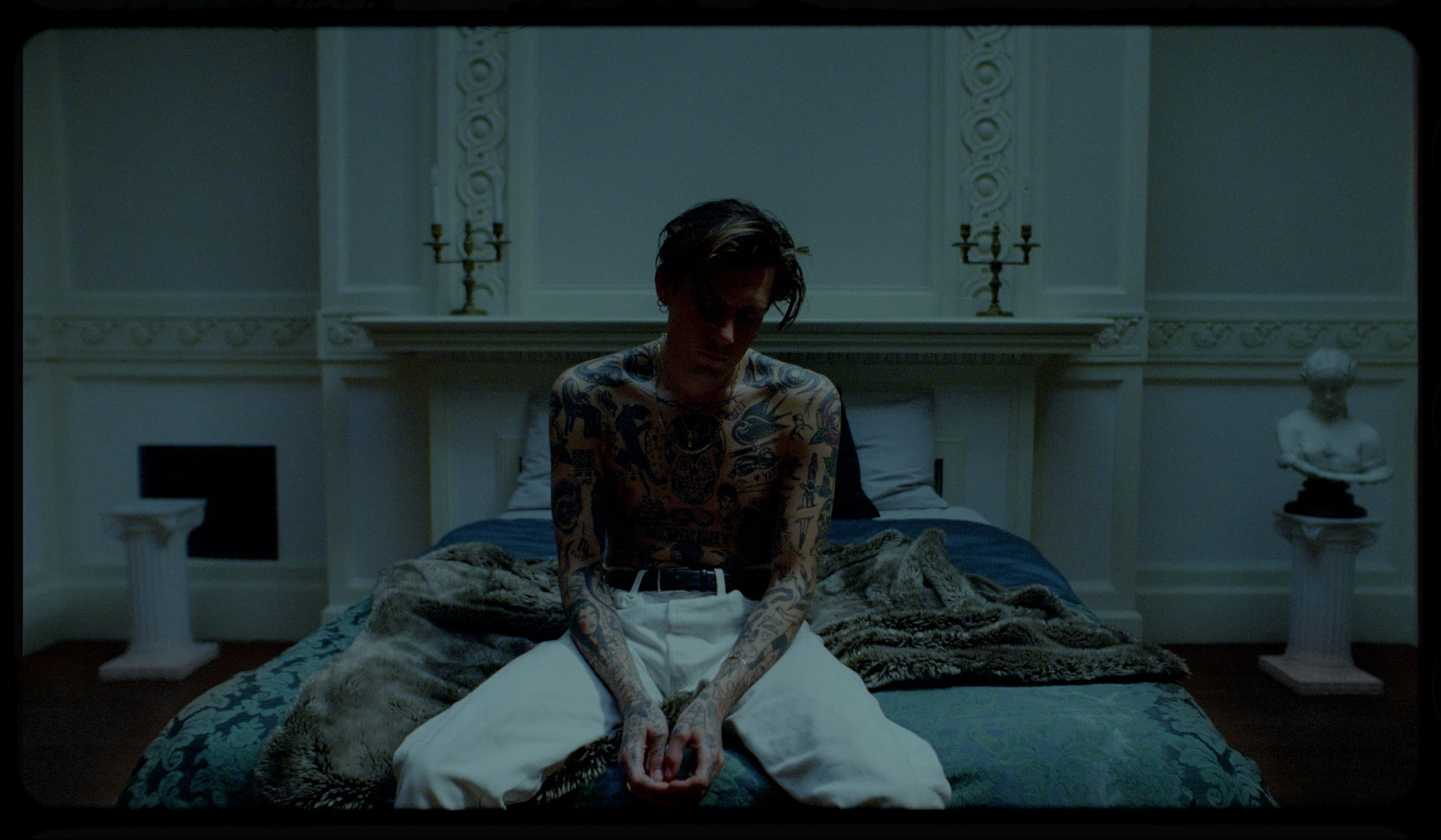 a tattooed man sitting on a bed in a room