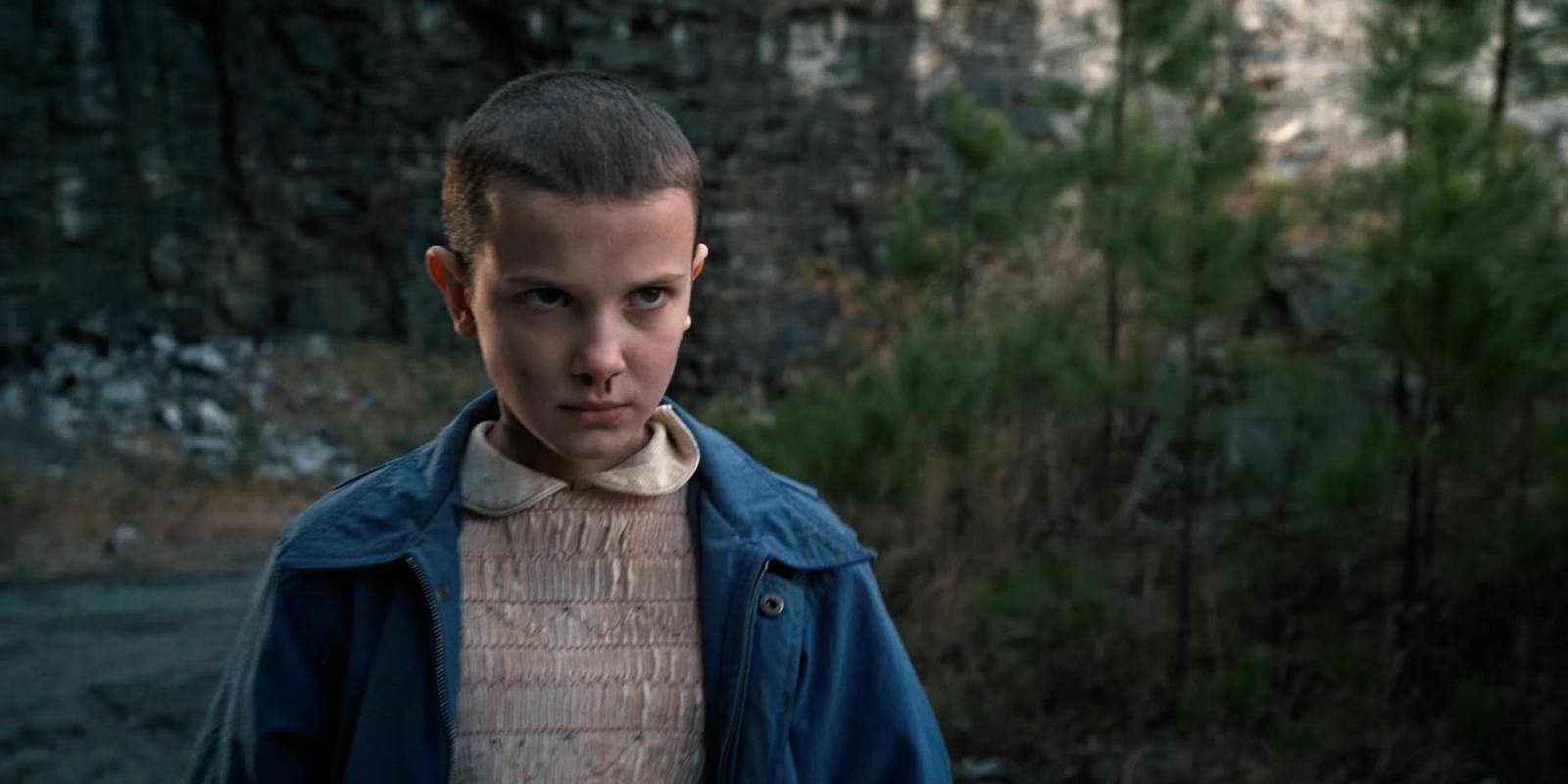 a boy in a blue jacket standing in front of a forest